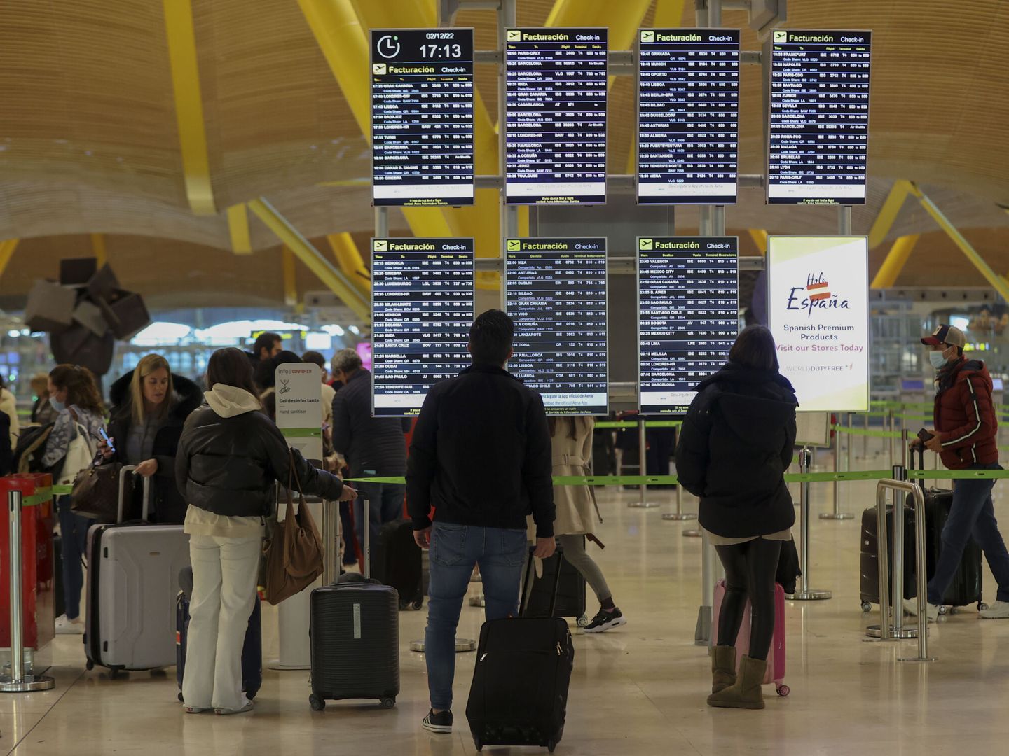 Varias personas observan paneles informativos en el interior de la terminal 4 del aeropuerto de Madrid-Barajas. (EFE/Kiko Huesca)