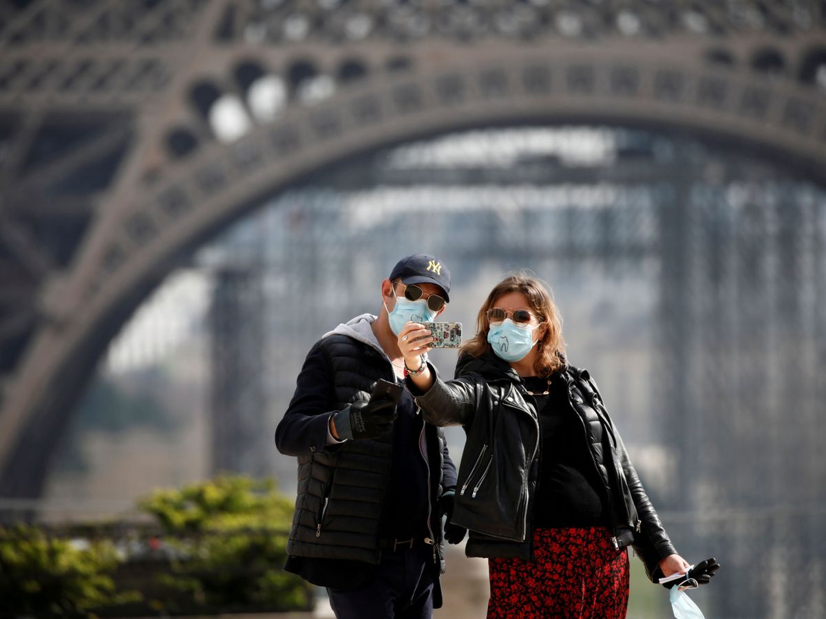 Foto: Dos turistas se fotografían con mascarillas en la Torre Eiffel. (Reuters)