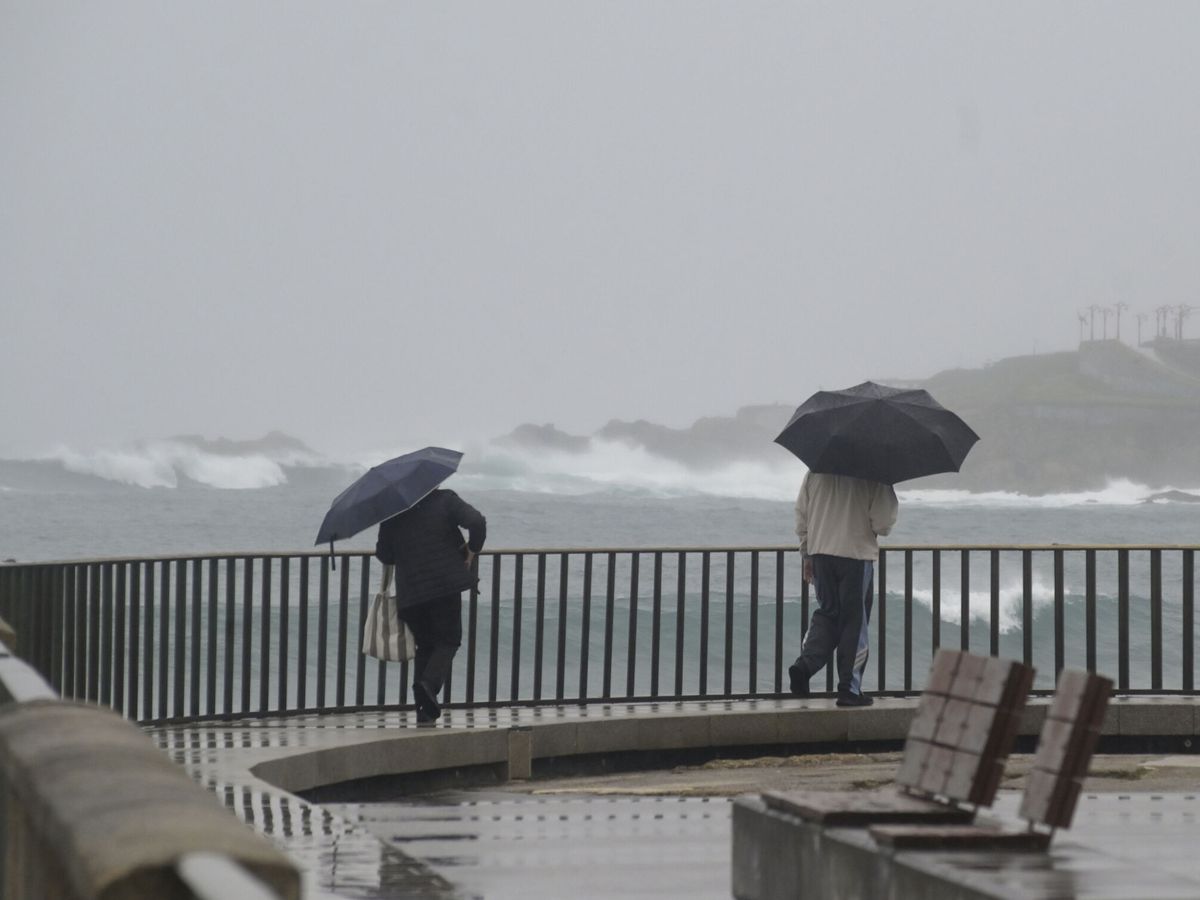 Foto: Dos personas caminan con un paraguas al lado de la playa del Orzán, en A Coruña. (Europa Press/M. Dylan)