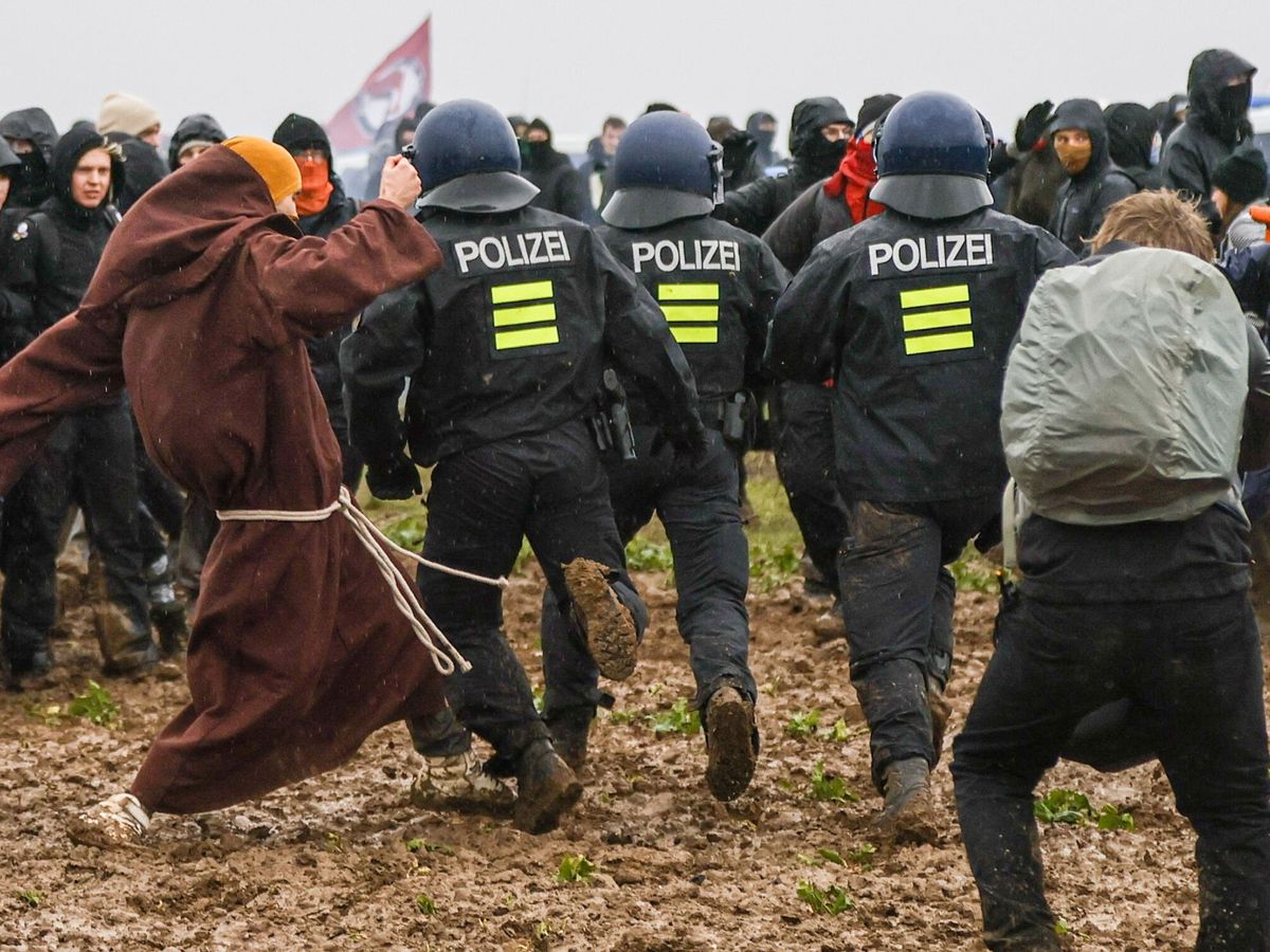 Foto: Un manifestante disfrazado de monje pone la zancadilla a un agente de policía durante los desalojos en Lutzerath, Alemania. (EFE/Ronald Wittek)