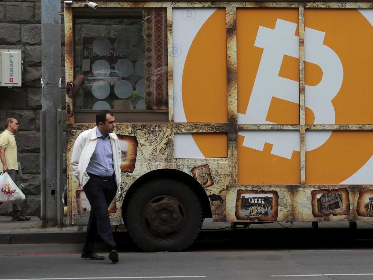 Foto: Un hombre pasa ante un cartel con el logo de bitcoin en una calle de Yerevan, en Armenia. (Reuters)