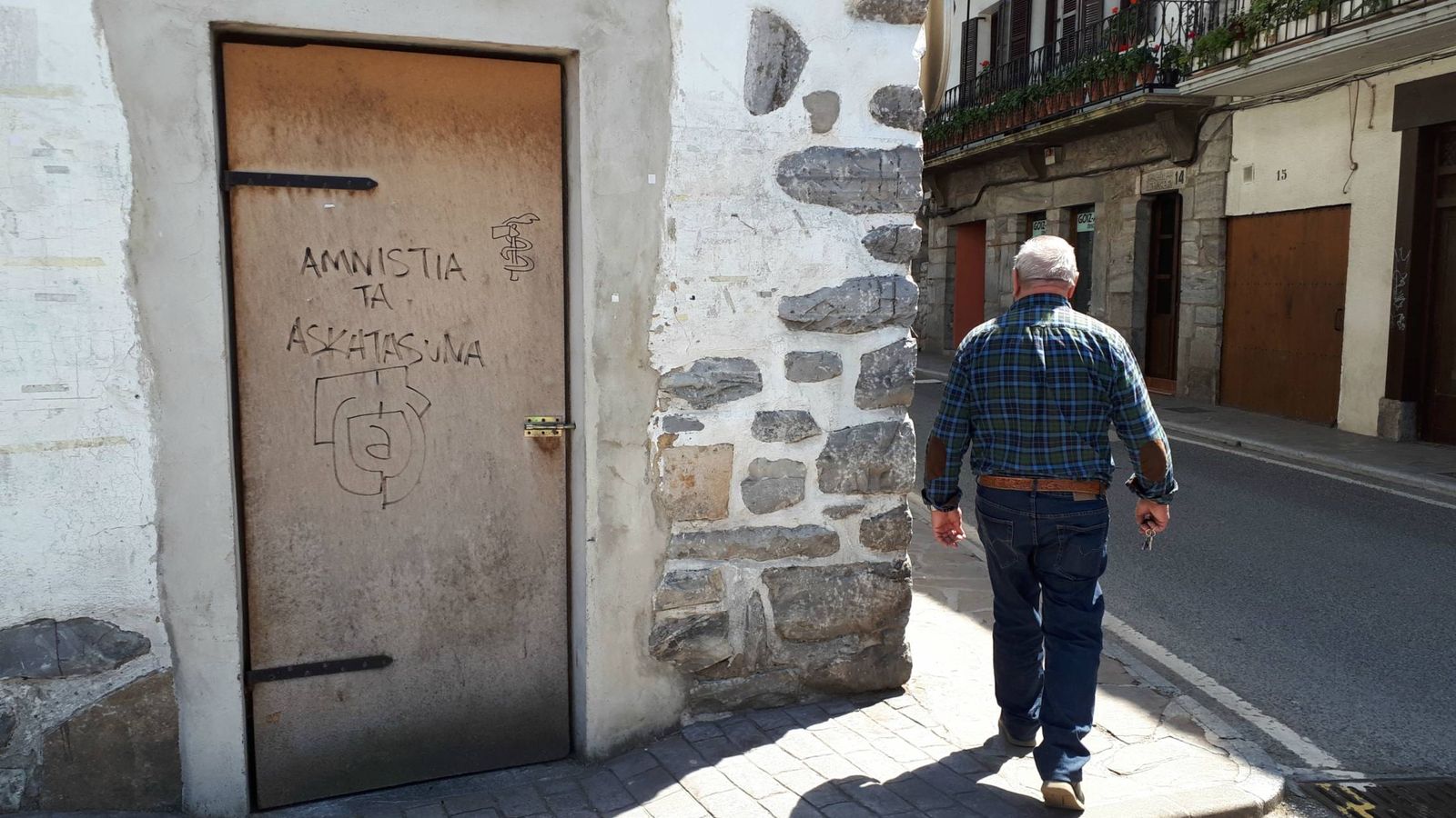 Foto: Un hombre pasa por delante de una puerta con una pintada con el símbolo de ETA que pide "amnistía" y "libertad" en Lesaka. (J. M. A.)
