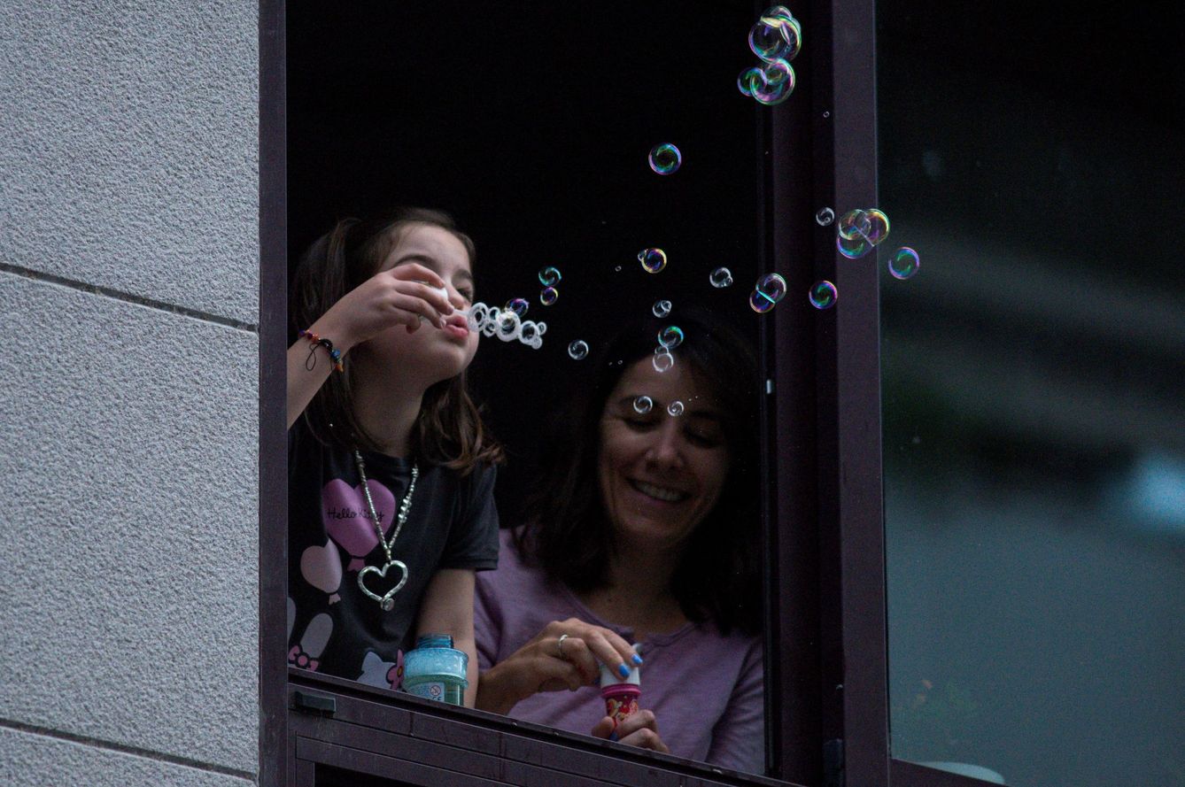 Una niña sopla pompas de jabón desde una ventana de su vivienda, ayer en Ourense. (EFE)