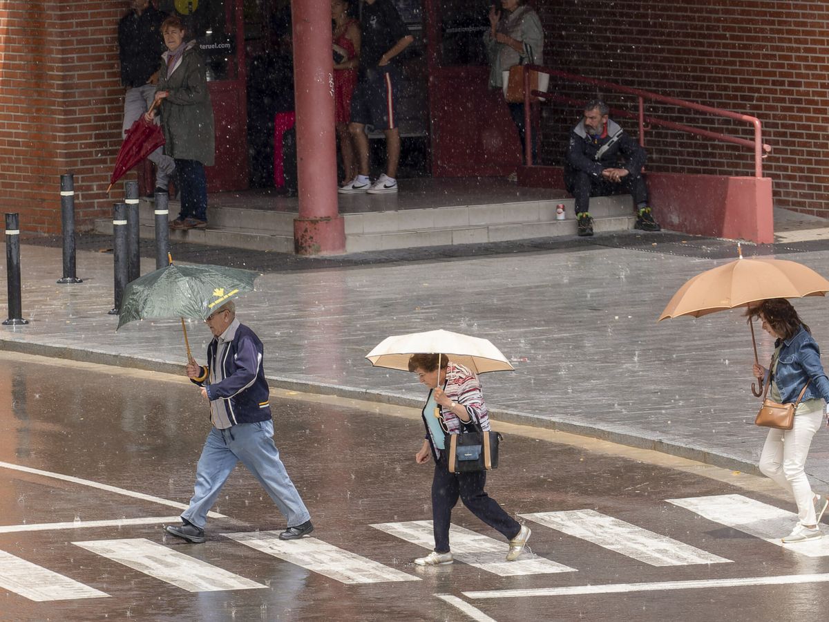 Foto: Varias personas caminan bajo la tormenta de este lunes, 12 de junio, en Teruel. (EFE/Antonio García)