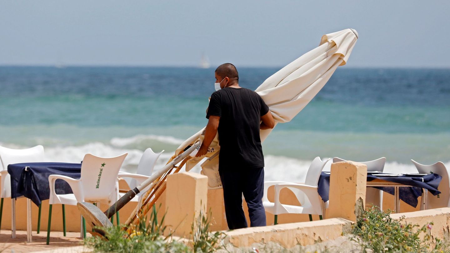 Un empleado de un restaurante protegido con mascarilla mueve una sombrilla en la playa de El Saler. (EFE)