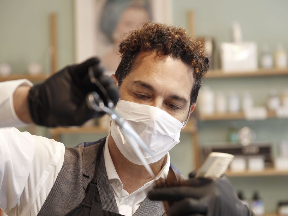Foto: Un peluquero corta el cabello a una cliente protegido con guantes y mascarilla (EFE)