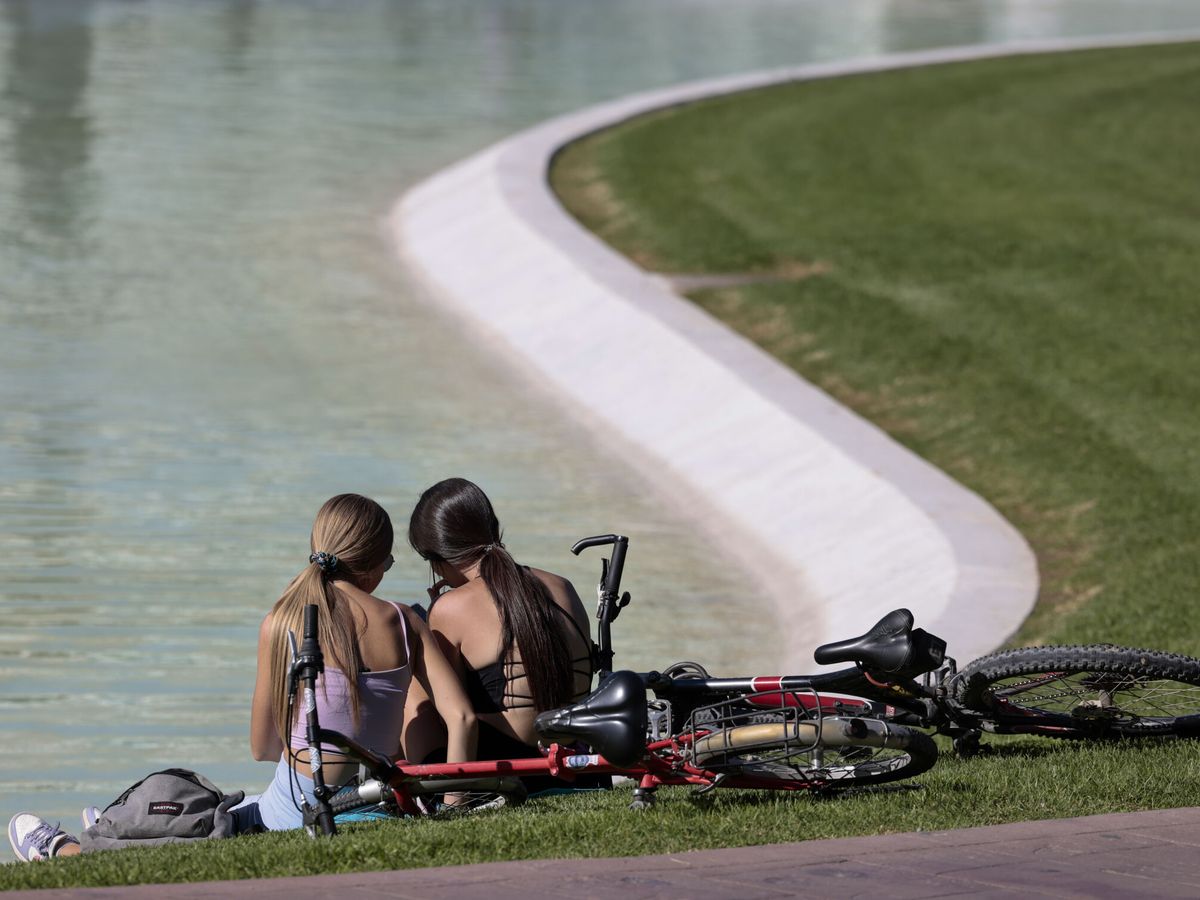 Foto: Dos jóvenes descansan junto a un estanque en Valencia. (EFE/Ana Escobar)