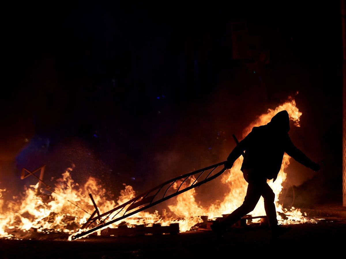 Foto: Un manifestante lanza una valla a la barricada en llamas en la calle Aragó en las protestas por el encarcelamiento de Pablo Hasél. (EFE)
