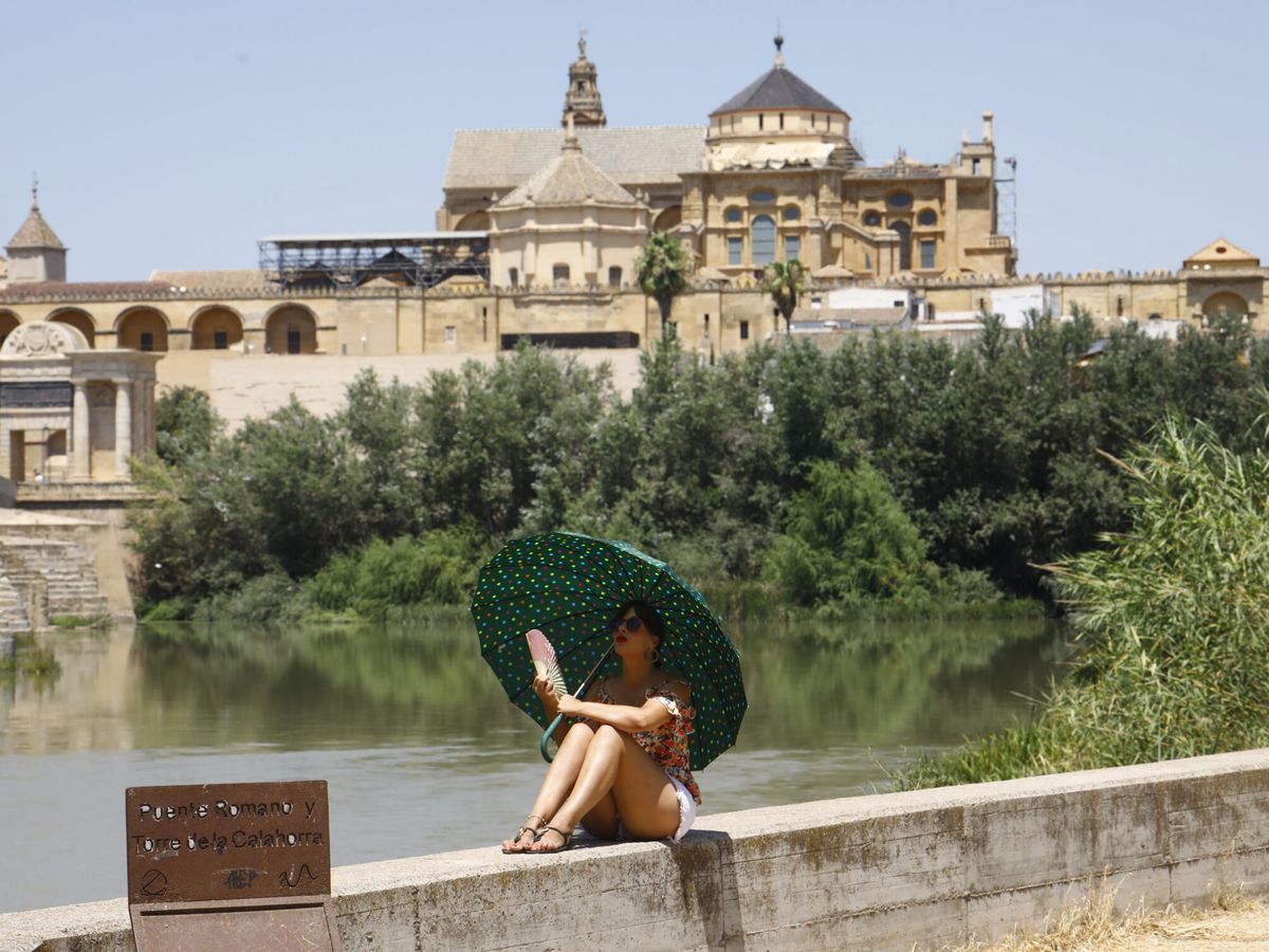 Foto: Una turista se protege del calor con un paraguas y un abanico a la orilla del río Guadalquivir cerca de la Mezquita-Catedral de Córdoba. (EFE/Salas)