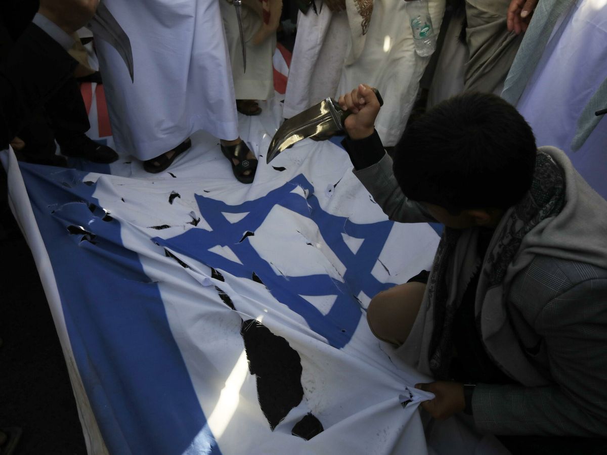 Foto: Un hombre usa un cuchillo para dañar una bandera israelí durante una manifestación para protestar por los bombardeos de Estados Unidos y Reino Unido sobre bases militares hutíes. (EFE/Yahya Arhab)