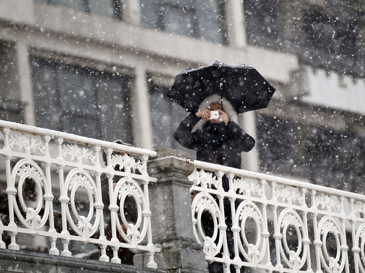 Una persona hace una foto junto a la barandilla de La Concha en una jornada de nieve. (EFE)