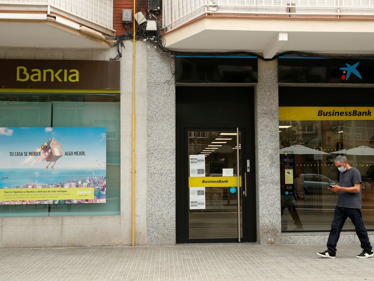 Foto: Un hombre camina delante de sucursales de CaixaBank y de Bankia. (Reuters)