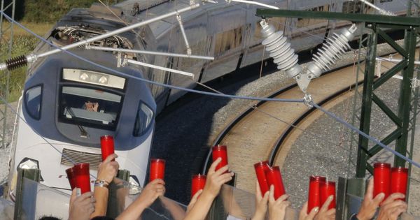 Foto: Los vecinos de Angrois alzan los cirios, mientras el conductor los saluda, al paso tren que hace la ruta del que descarriló en 2013. (EFE)