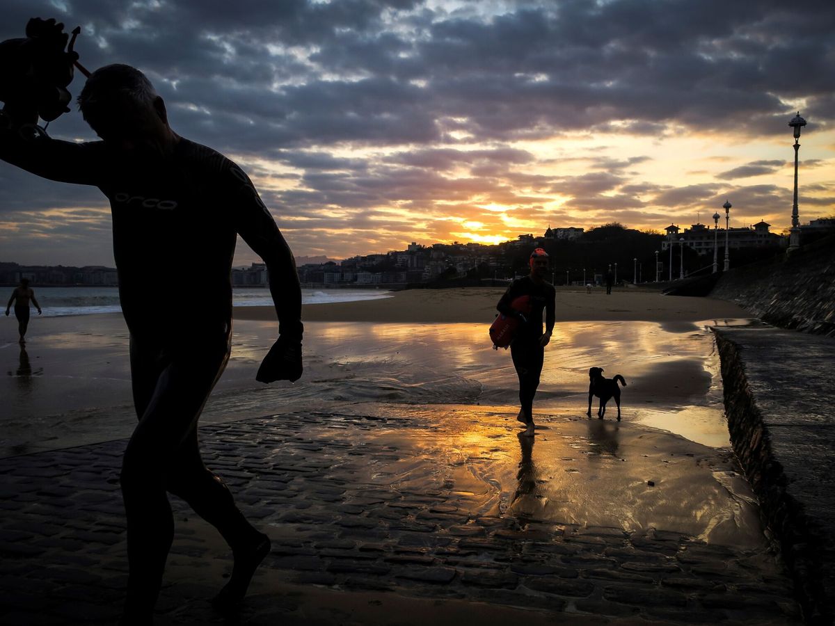 Foto: Dos hombres salen del agua al amanecer en la playa de Ondarreta. (EFE/Javier Etxezarreta)