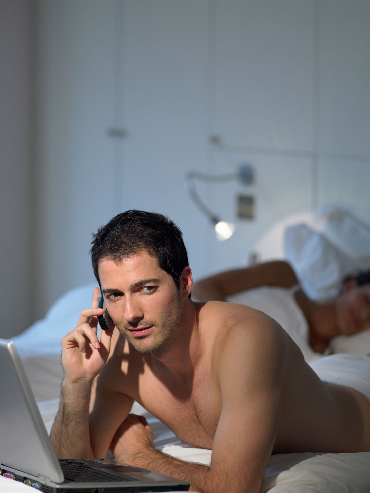 Man on cellphone as wife sleeps --- Image by © Image Source/Corbis